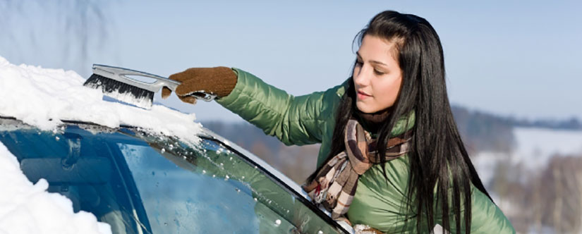 Woman scraping ice off car with a brush