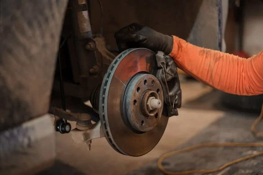 a mechanic checks the brake pads and discs of a vehicle in a garage.