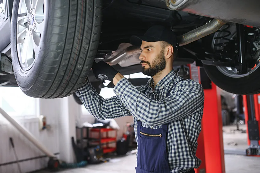 a mechanic works on the underside of a car in a garage.