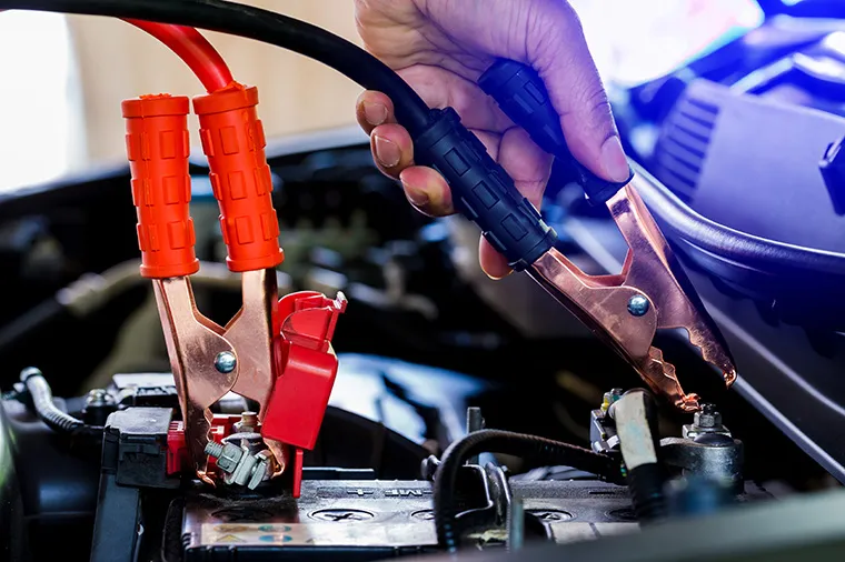 Hands disconnect positive and negative terminals in order to charge a car battery.